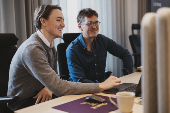 Two men collaborating at a desk with a laptop and a monitor