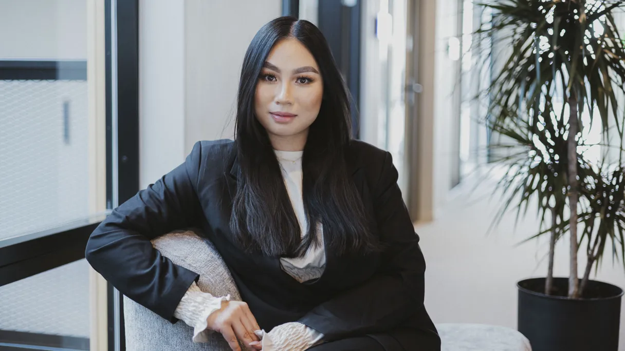 A woman in a black suit sitting on a chair in an office setting